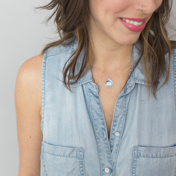 close up photo of brunette woman wearing inspirational necklace and jean shirt